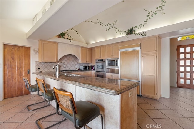 kitchen with vaulted ceiling, built in appliances, sink, kitchen peninsula, and light tile patterned flooring