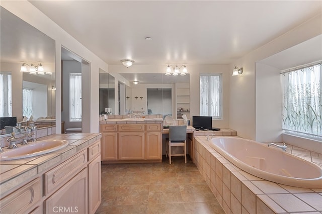 bathroom with tiled bath, vanity, a notable chandelier, and a wealth of natural light