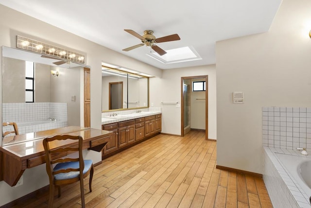 bathroom with a skylight, hardwood / wood-style floors, a relaxing tiled tub, ceiling fan, and vanity