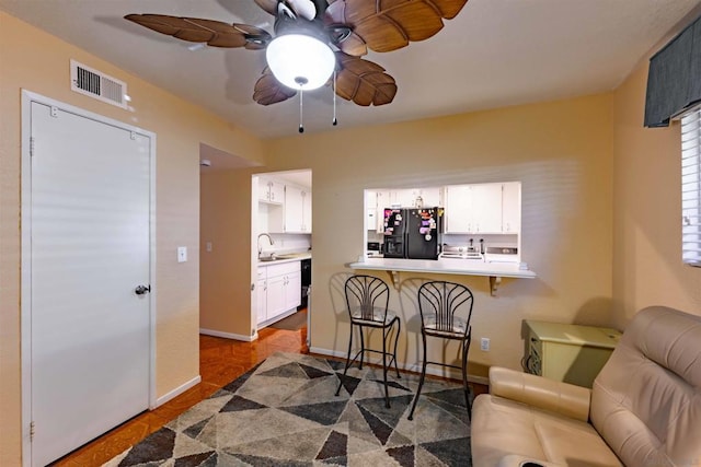 kitchen featuring black refrigerator with ice dispenser, kitchen peninsula, sink, white cabinetry, and a kitchen breakfast bar