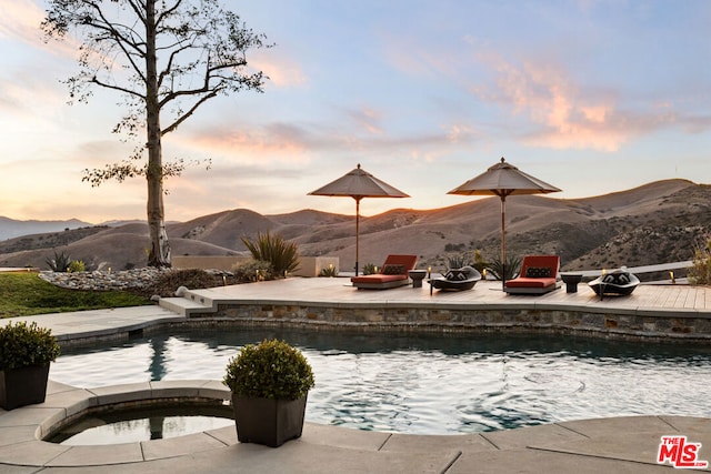 pool at dusk featuring a mountain view, a patio area, an in ground hot tub, and a fire pit