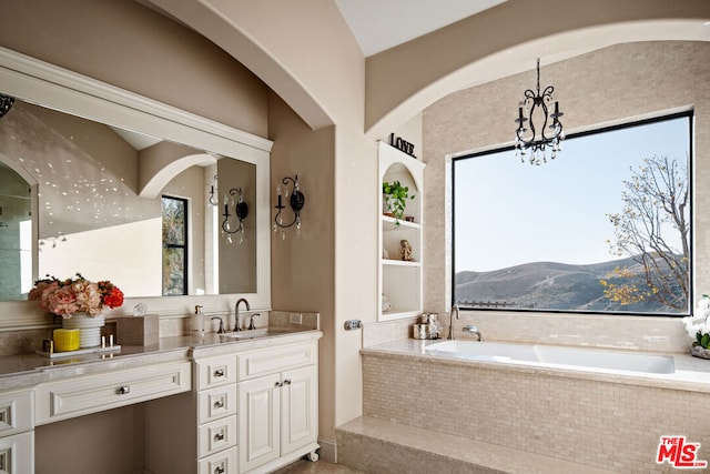 bathroom with an inviting chandelier, a mountain view, a relaxing tiled tub, vanity, and built in shelves