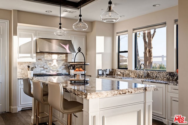 kitchen with exhaust hood, light stone countertops, white cabinetry, and a kitchen island