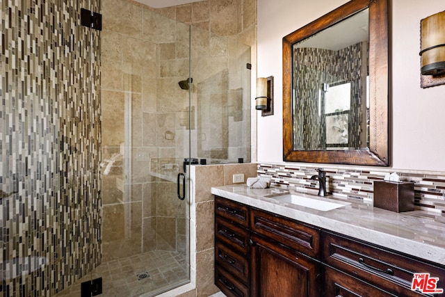 bathroom with a shower with shower door, vanity, and tasteful backsplash