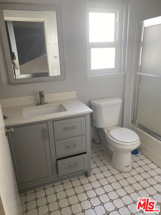 full bathroom featuring vanity, enclosed tub / shower combo, and toilet