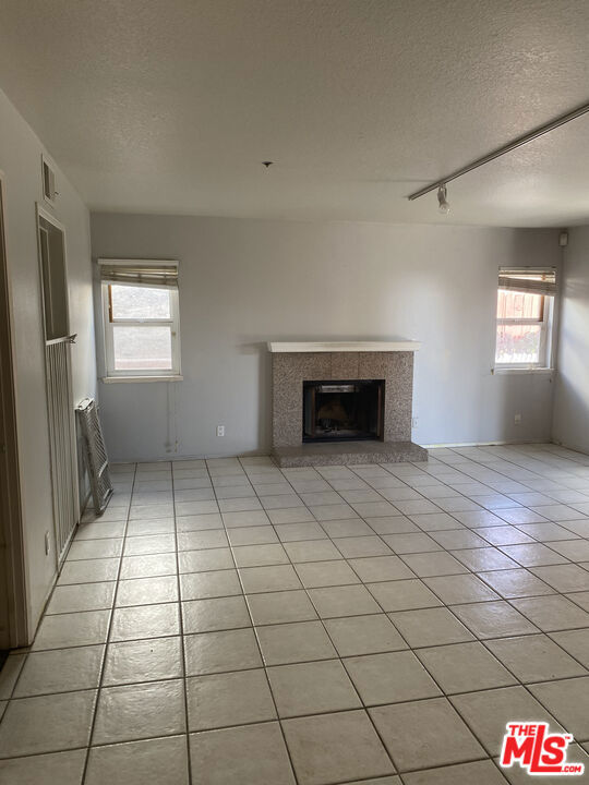 unfurnished living room featuring track lighting, a tile fireplace, a textured ceiling, and light tile patterned flooring