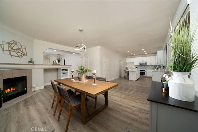 dining space with a fireplace, baseboards, crown molding, and wood finished floors