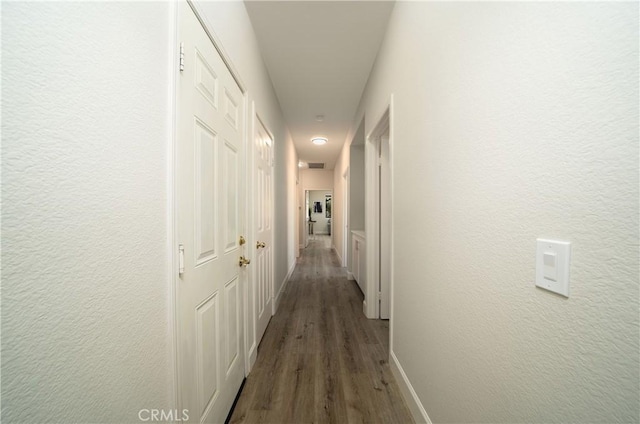 hallway with dark wood-style floors, visible vents, baseboards, and a textured wall