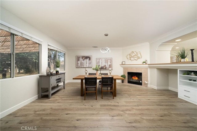 dining space with ornamental molding, a tile fireplace, baseboards, and wood finished floors