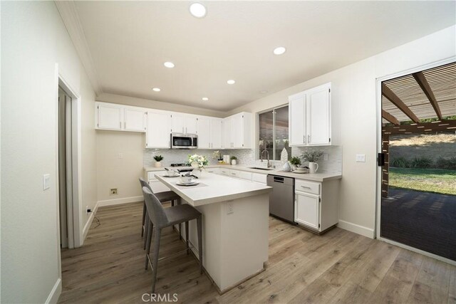 kitchen with a breakfast bar, a center island, stainless steel appliances, light countertops, and white cabinetry