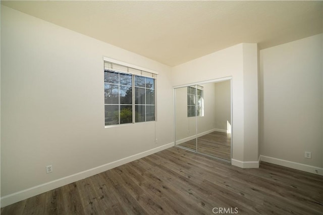 unfurnished bedroom with a closet, baseboards, and dark wood-type flooring