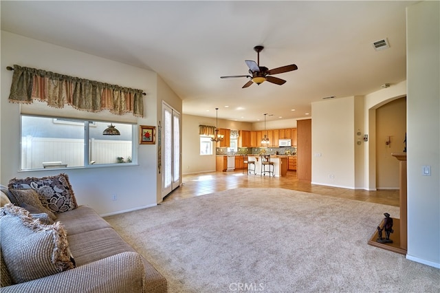 carpeted living room with ceiling fan with notable chandelier