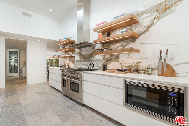 kitchen with white cabinets, appliances with stainless steel finishes, a towering ceiling, island exhaust hood, and tasteful backsplash