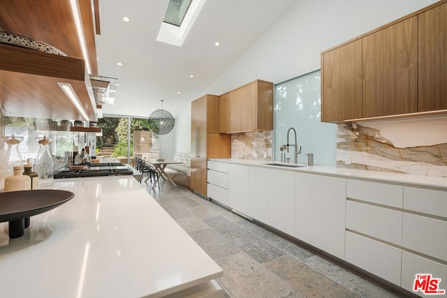 kitchen featuring backsplash, sink, hanging light fixtures, a skylight, and white cabinets