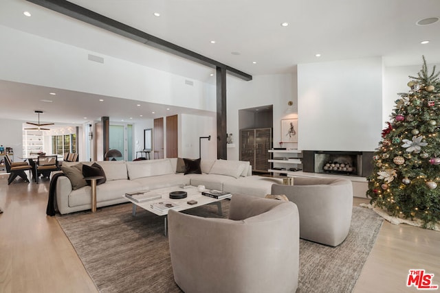 living room featuring ceiling fan, a high ceiling, light hardwood / wood-style flooring, and beamed ceiling