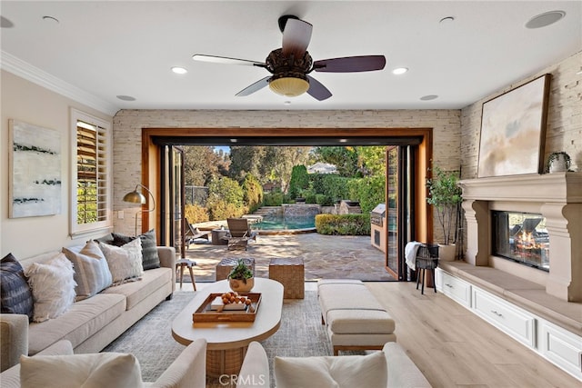 living room featuring ceiling fan, a large fireplace, crown molding, and light hardwood / wood-style floors