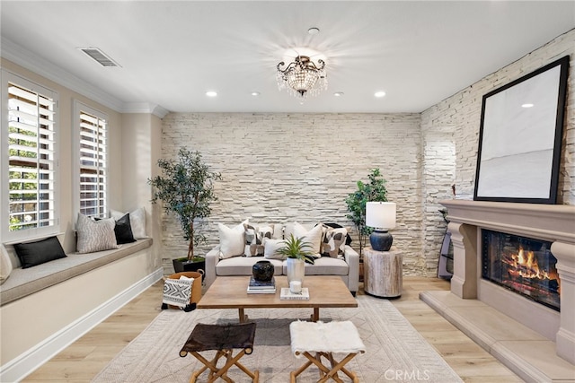 living room with crown molding, a fireplace, a notable chandelier, and light hardwood / wood-style floors