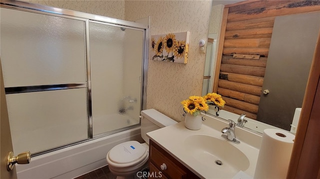 full bathroom with rustic walls, shower / bath combination with glass door, vanity, and toilet