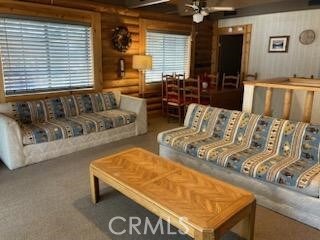 carpeted living room featuring ceiling fan and log walls