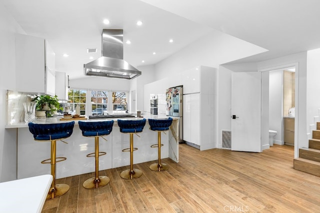 kitchen featuring visible vents, island range hood, freestanding refrigerator, a peninsula, and white cabinetry