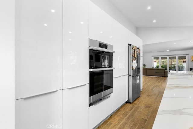 kitchen featuring light stone counters, modern cabinets, appliances with stainless steel finishes, white cabinetry, and wood finished floors