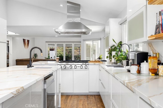 kitchen with light stone counters, white cabinets, a sink, and island range hood