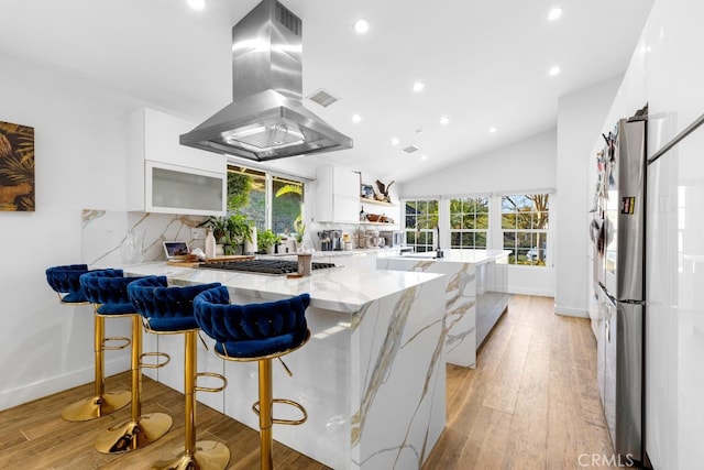 kitchen featuring island range hood, a peninsula, a breakfast bar, white cabinetry, and open shelves