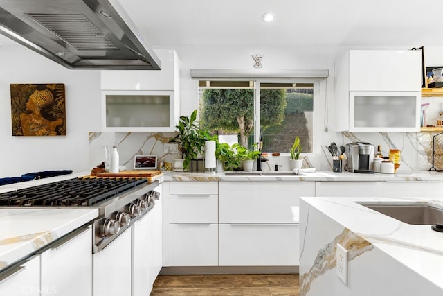 kitchen with wall chimney exhaust hood, light wood-style floors, backsplash, and white cabinets