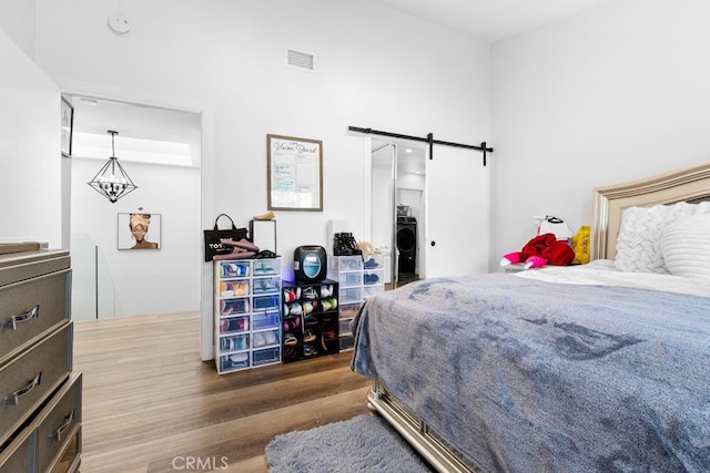 bedroom featuring a barn door, washer / dryer, wood finished floors, and visible vents