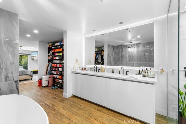 full bath featuring double vanity, connected bathroom, wood finished floors, a spacious closet, and a sink