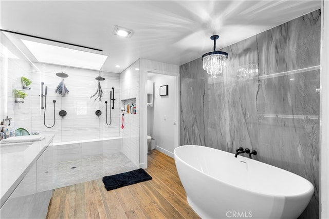 bathroom with wood finished floors, a freestanding bath, vanity, a walk in shower, and tile walls