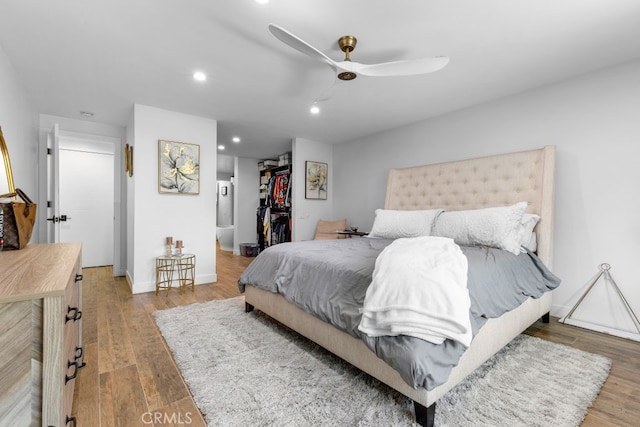 bedroom with baseboards, a walk in closet, wood finished floors, and recessed lighting