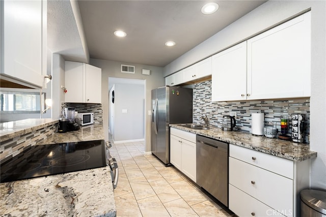 kitchen with tasteful backsplash, white cabinets, appliances with stainless steel finishes, and light stone counters