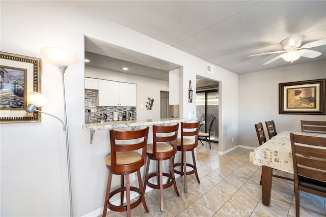 kitchen with white cabinetry, kitchen peninsula, ceiling fan, tasteful backsplash, and a kitchen breakfast bar