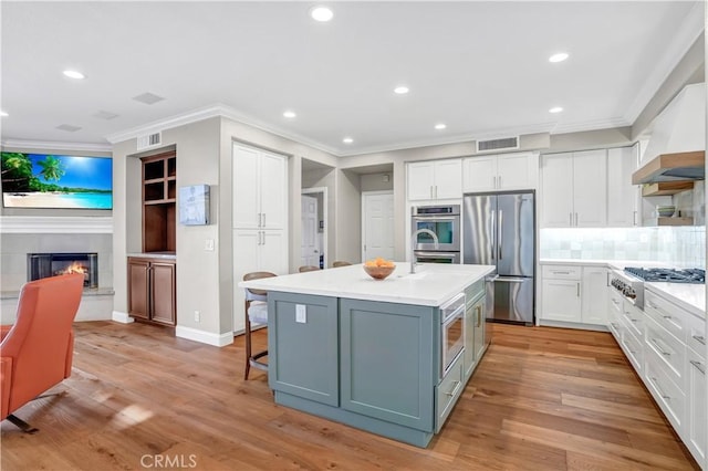 kitchen featuring appliances with stainless steel finishes, white cabinetry, decorative backsplash, a center island with sink, and light wood-type flooring