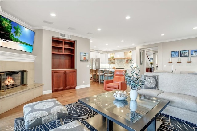 living room featuring sink, light hardwood / wood-style flooring, ornamental molding, and a premium fireplace