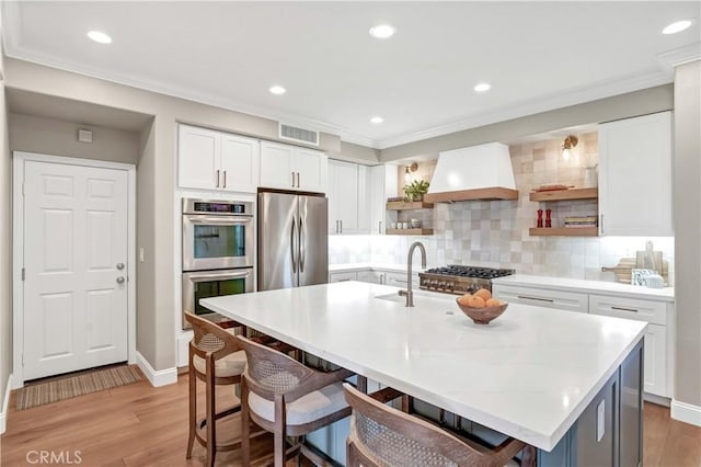 kitchen featuring backsplash, stainless steel appliances, custom range hood, and a center island with sink