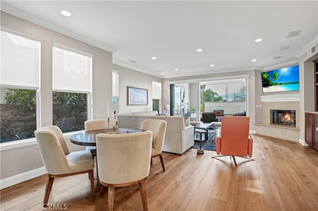 dining space with a tiled fireplace, crown molding, plenty of natural light, and light hardwood / wood-style floors