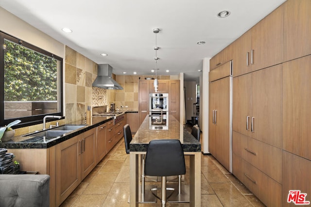 kitchen featuring a kitchen island, sink, a kitchen bar, hanging light fixtures, and wall chimney range hood