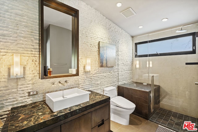 bathroom featuring tile walls, vanity, a tile shower, tile patterned floors, and toilet