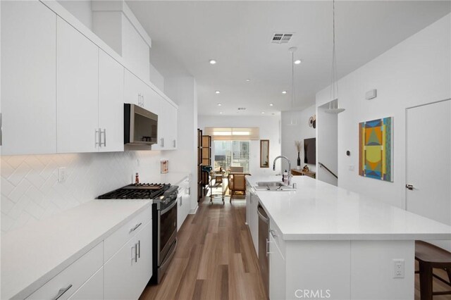 kitchen featuring a kitchen breakfast bar, white cabinetry, appliances with stainless steel finishes, and a center island with sink