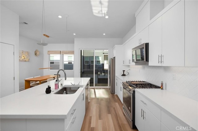 kitchen featuring white cabinetry, a center island with sink, appliances with stainless steel finishes, decorative backsplash, and sink