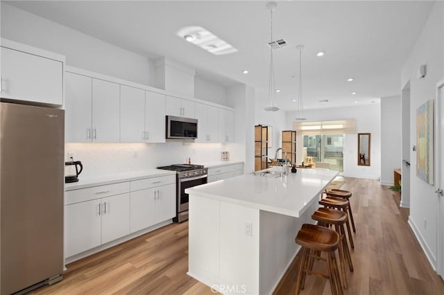 kitchen featuring appliances with stainless steel finishes, a center island with sink, white cabinets, a kitchen bar, and decorative light fixtures