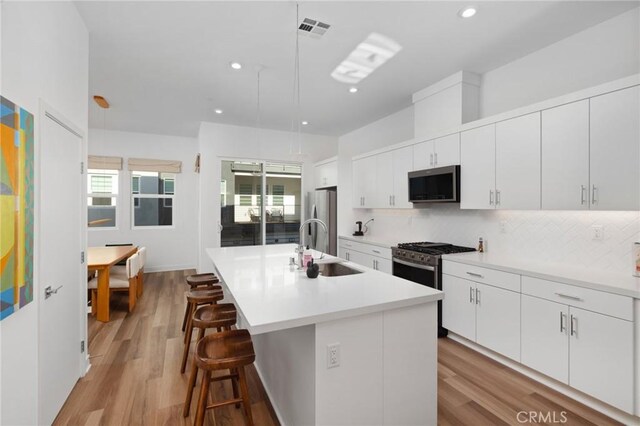 kitchen featuring appliances with stainless steel finishes, white cabinets, hanging light fixtures, and a kitchen island with sink