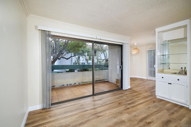 unfurnished dining area with baseboards, crown molding, a textured ceiling, light wood-style floors, and a sink