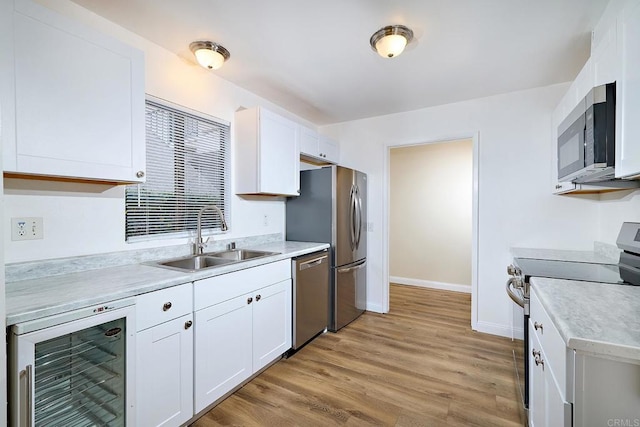 kitchen with beverage cooler, stainless steel appliances, a sink, white cabinetry, and light wood finished floors