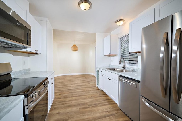 kitchen with light wood-style flooring, stainless steel appliances, a sink, white cabinets, and light countertops