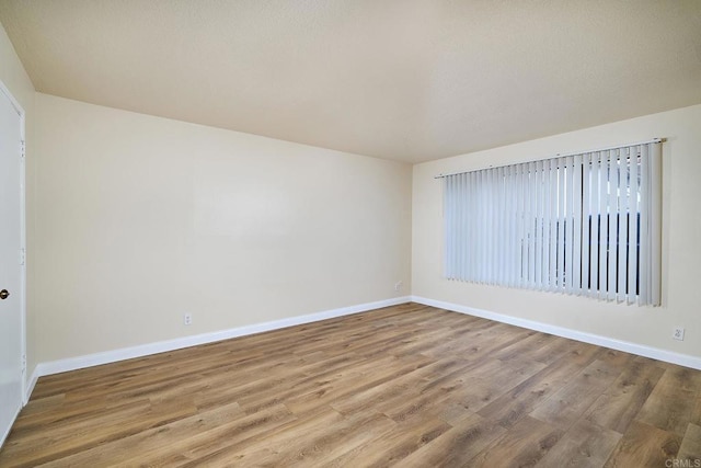 spare room with baseboards and wood finished floors