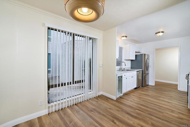 kitchen with light countertops, light wood-style floors, white cabinetry, a sink, and baseboards