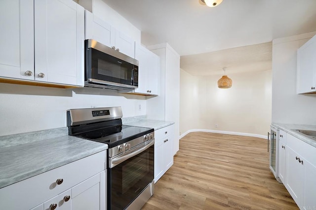 kitchen featuring baseboards, light wood-style flooring, appliances with stainless steel finishes, light countertops, and white cabinetry